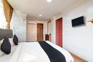 A hotel room with a bed, a TV mounted on the wall, an air conditioning unit, and a wooden door. - Raj Palace- by Brill Rooms (Barasat)