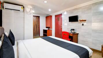 Habitación de hotel con cama, escritorio, silla, televisor y aire acondicionado.