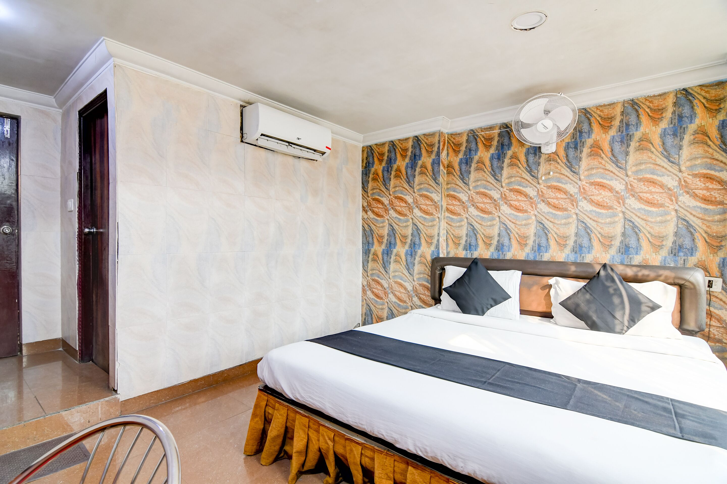 A hotel room with a bed, an air conditioning unit, a ceiling fan, and a patterned wall.