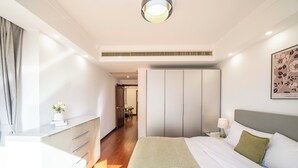 A modern hotel room with a large bed, a bedside table with a lamp, a wardrobe, and a small desk with drawers. - Tyms Gubei Apt 2BR Residence near Gubei (Shanghai)