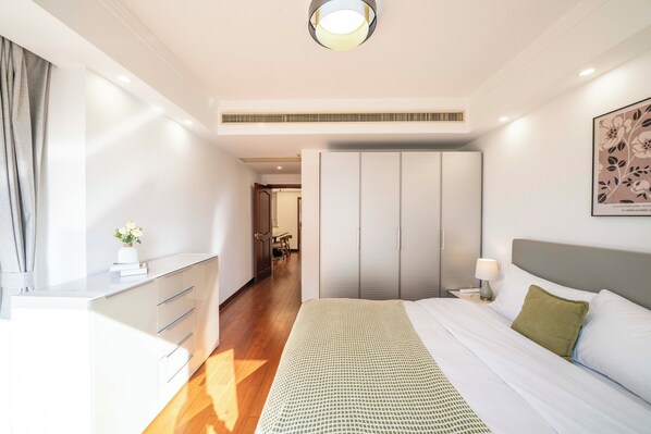 Une chambre d’hôtel moderne avec un grand lit, une table de chevet avec une lampe, une armoire et un petit bureau avec des tiroirs.