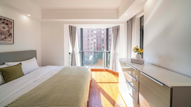 A bedroom with a bed, a dresser, a window with curtains, and a view of buildings. - Tyms Gubei Apt 2BR Residence near Gubei (Shanghai)