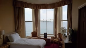 Habitación de hotel con dos camas, un escritorio, una silla, un ventilador y vista al mar.