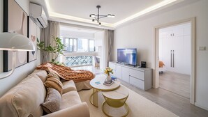 Un salon moderne avec un canapé, une table basse et un téléviseur. Il y a un balcon avec vue sur la ville.