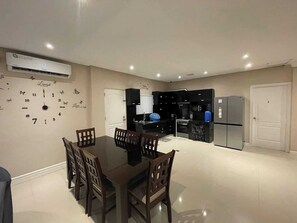 A dining area with a table and chairs, a kitchen with black cabinets, a refrigerator, and an air conditioning unit. - Charming 3-Bedroom House Rental in Camarines Norte (Camarines Norte)