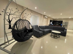 Un salon moderne avec un canapé d’angle gris, un fauteuil suspendu et une petite table ronde.