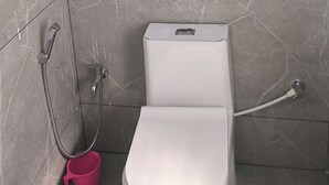 Un baño con inodoro, ducha y un cubo rosa.