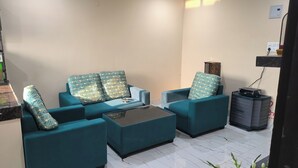 Una sala de estar con sofás color turquesa, una mesa de centro de vidrio y un altavoz negro.