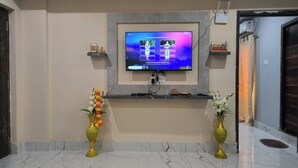 Sala de estar con un televisor de pantalla plana montado en una pared de mármol, dos jarrones decorativos a cada lado y una estantería con objetos pequeños.