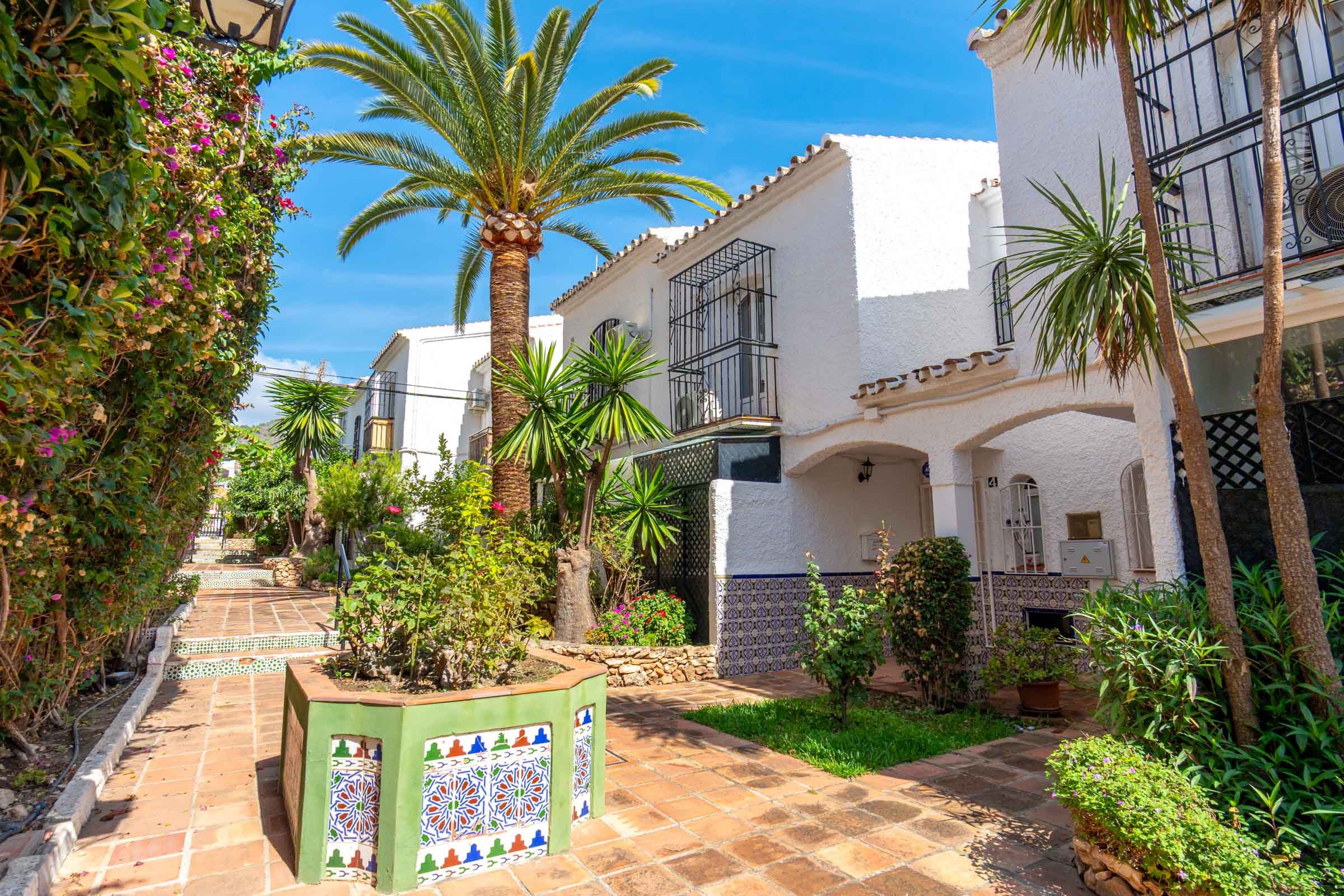 A courtyard with a tiled pathway, palm trees, and a building with balconies.
