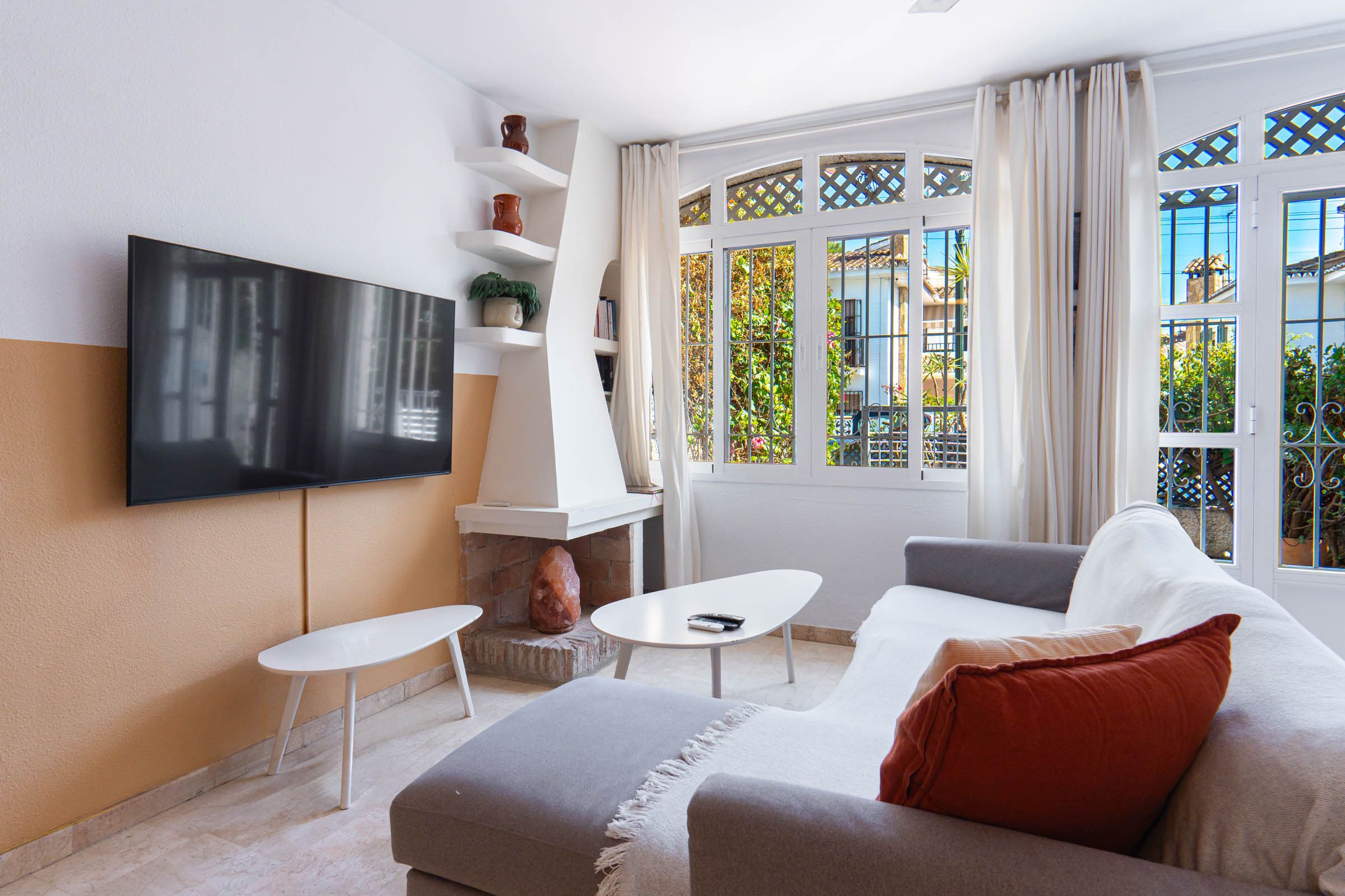 Un salon moderne doté d’un téléviseur à écran plat fixé au mur, d’une cheminée, d’un canapé, d’une table basse et offrant une vue sur l’extérieur grâce à de grandes fenêtres.
