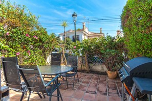 A patio with a table and chairs, a barbecue grill, and a view of a building in the background. - Summer Azul 3 Casa Lena by Casasol (Nerja)