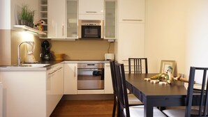 Una cocina compacta con armarios blancos, un horno integrado y una mesa con sillas.
