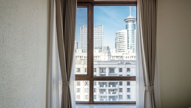 A hotel room with a large window offering a view of a city skyline, including a distinctive tower. - Tyms Gubei Apt 2BR near Metro Plaza (Shanghai)
