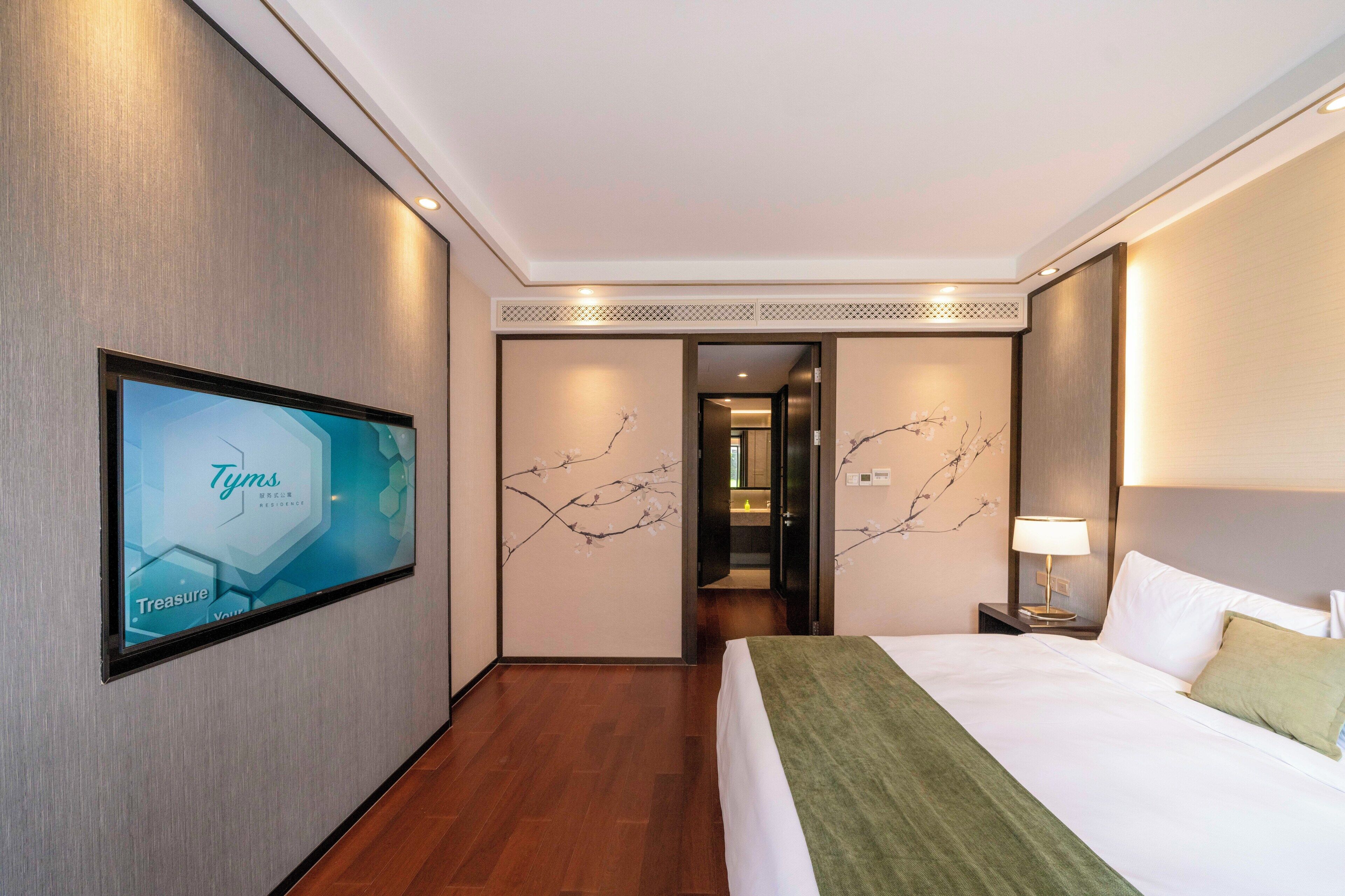 A hotel room with a bed, a TV mounted on the wall, and a door leading to another room.