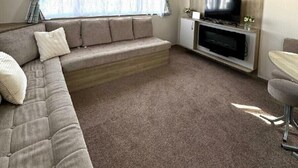 Ein modernes Wohnzimmer mit einem Ecksofa, einem Flachbildfernseher und einem kleinen Esstisch.