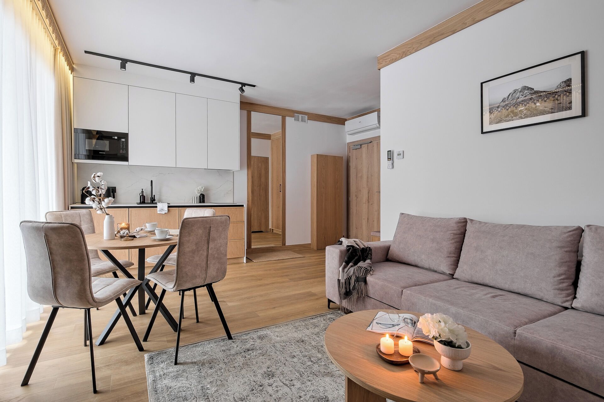 A modern living room with a sofa, a dining area with chairs, a kitchen with cabinets, and a framed picture on the wall.