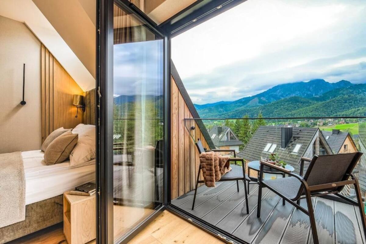 A bedroom with a large window, a bed, a bedside table, and a chair.