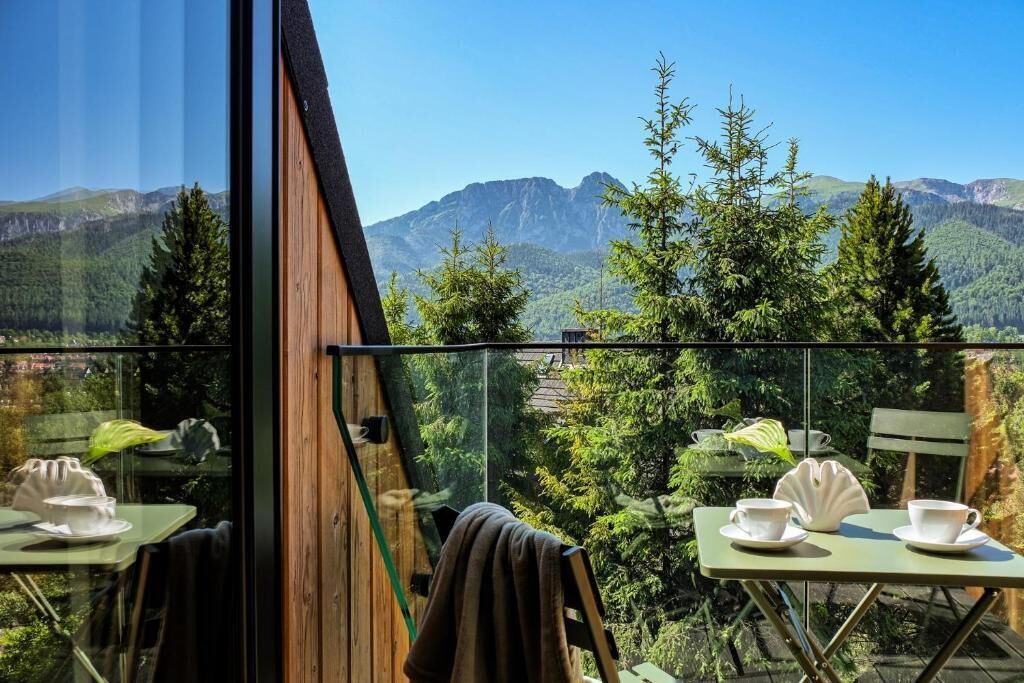 Comedor con vistas a la montaña, con dos mesas y sillas, y barandilla de cristal.
