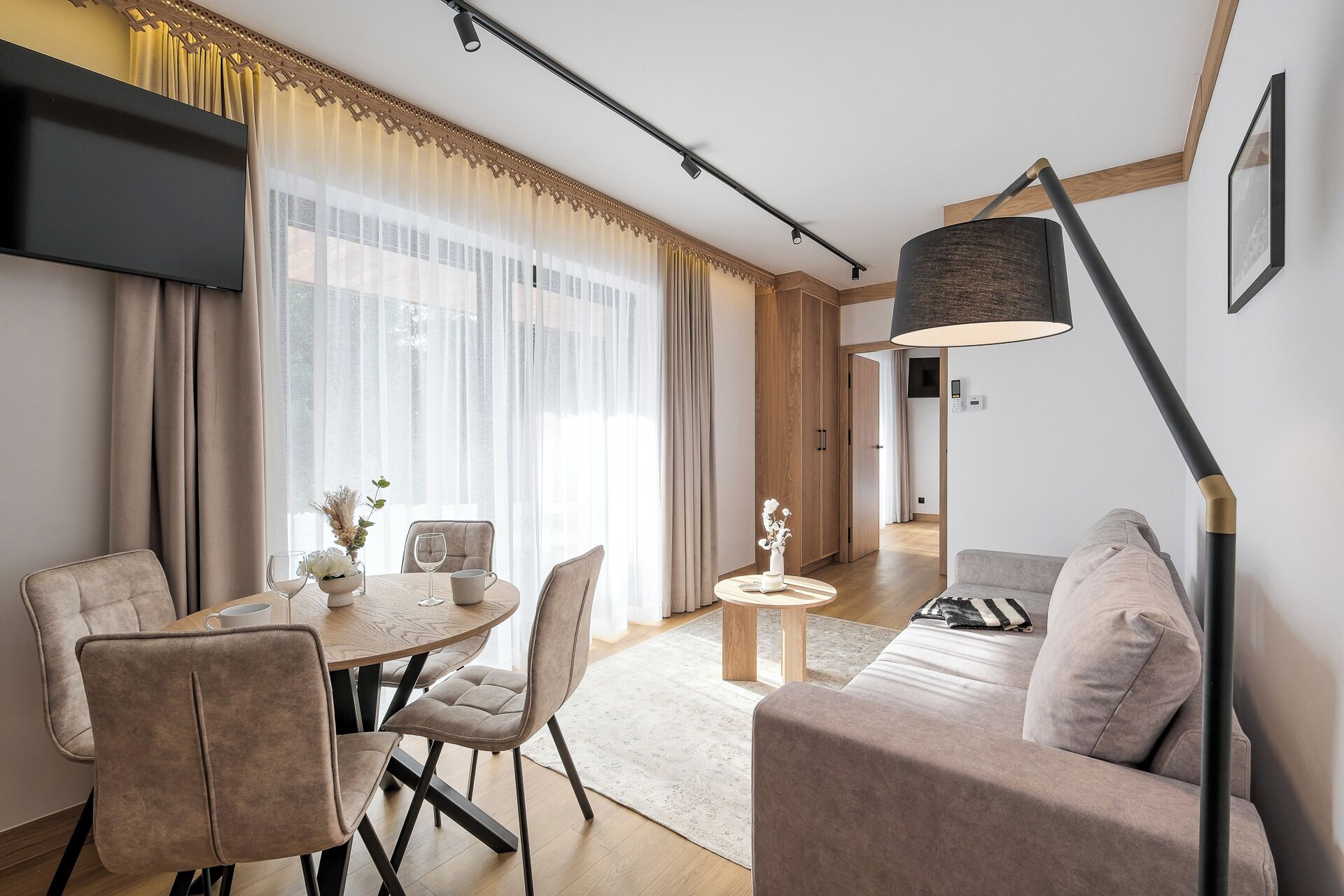 A modern living room with a sofa, a dining table with chairs, a TV, and a lamp.