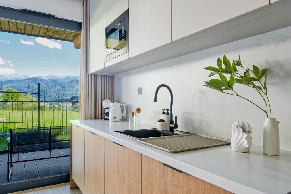 Una cocina moderna con un lavamanos integrado, una cafetera y vistas a un paisaje montañoso desde un balcón.