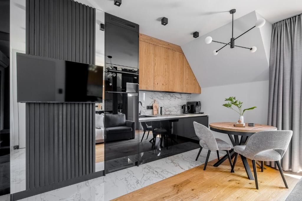 Una cocina moderna con una paleta de colores blanco y negro, un mueble de madera y un comedor con una mesa redonda y sillas.