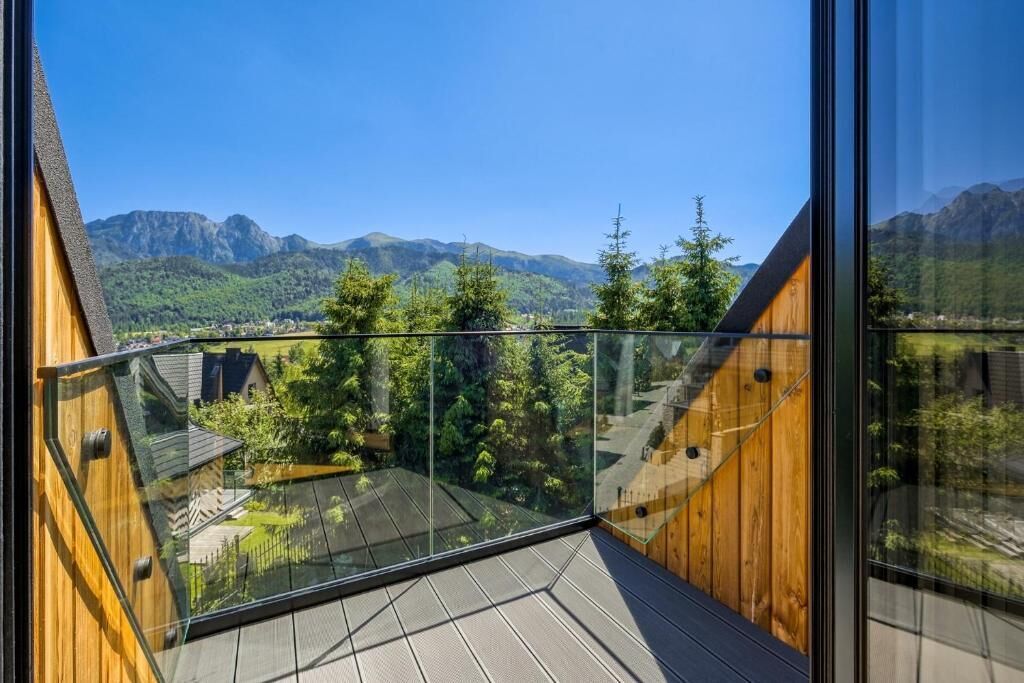A modern building with a glass balcony overlooking a mountainous landscape.