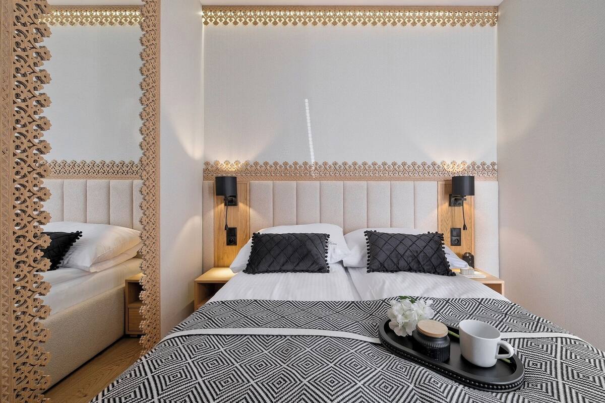 A hotel room with a large bed, two bedside tables, a mirror, and a decorative wooden headboard.