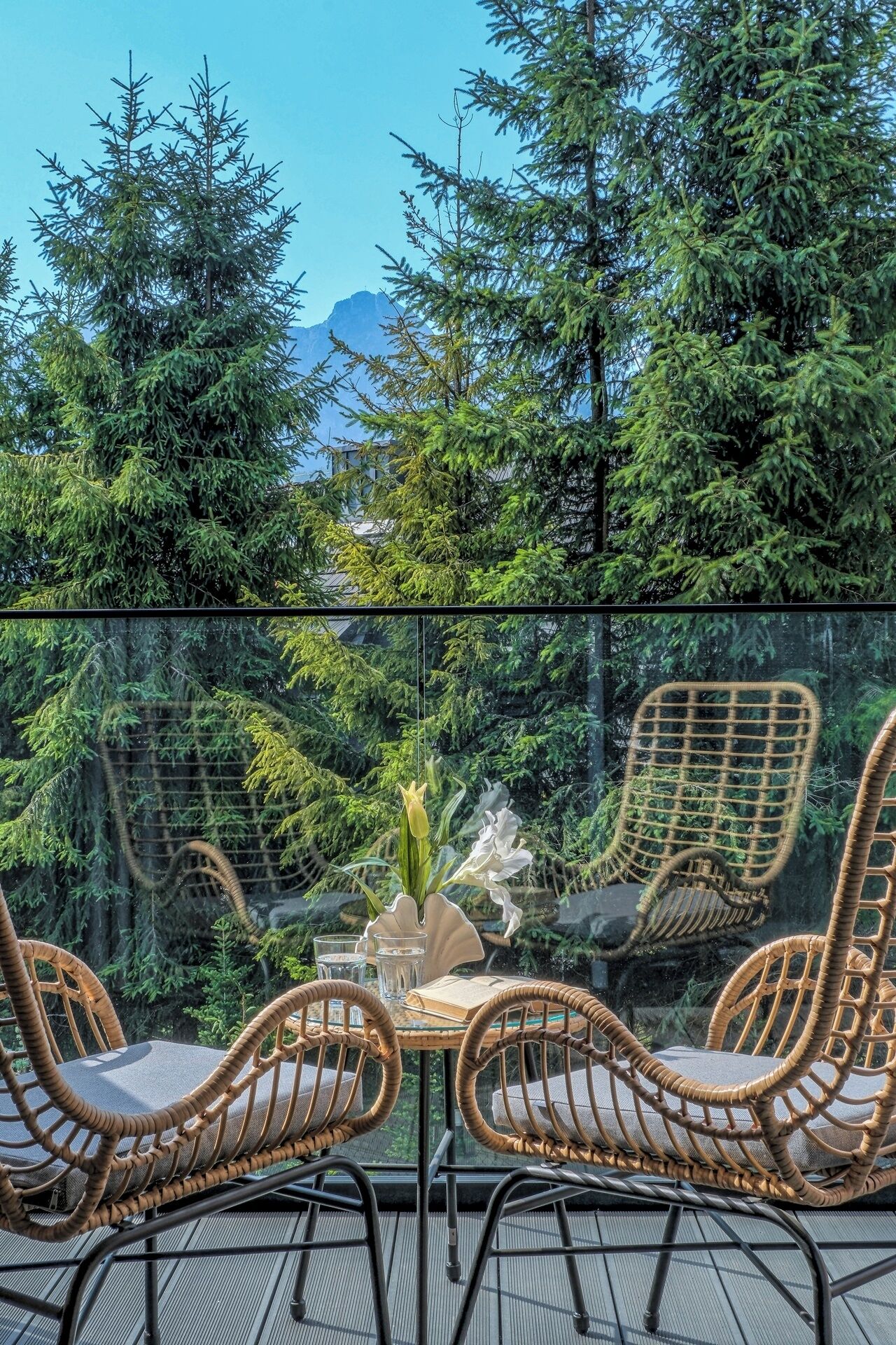 Ein überdachter Außenbereich mit Sitzgelegenheiten, darunter Korbstühle und ein Tisch, umgeben von üppiger Vegetation und Blick auf die Berge.