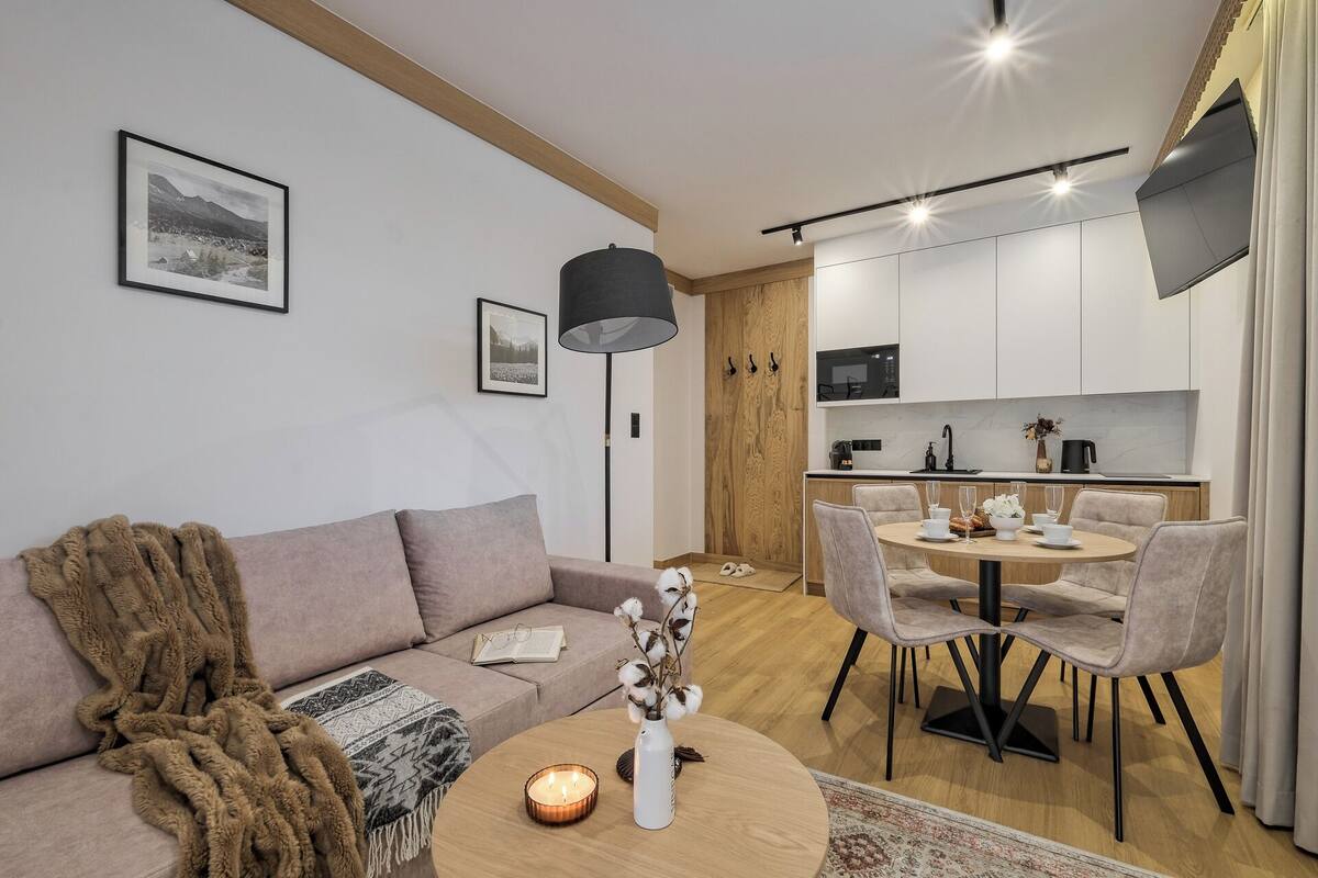 A modern living room with a sofa, a coffee table with a candle, and a dining area with chairs and a table set for a meal.