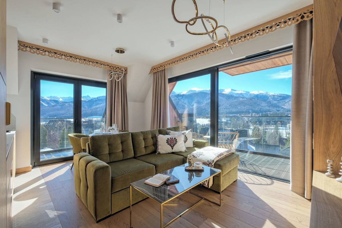 A modern living room with a sofa, coffee table, and large windows offering a mountain view.