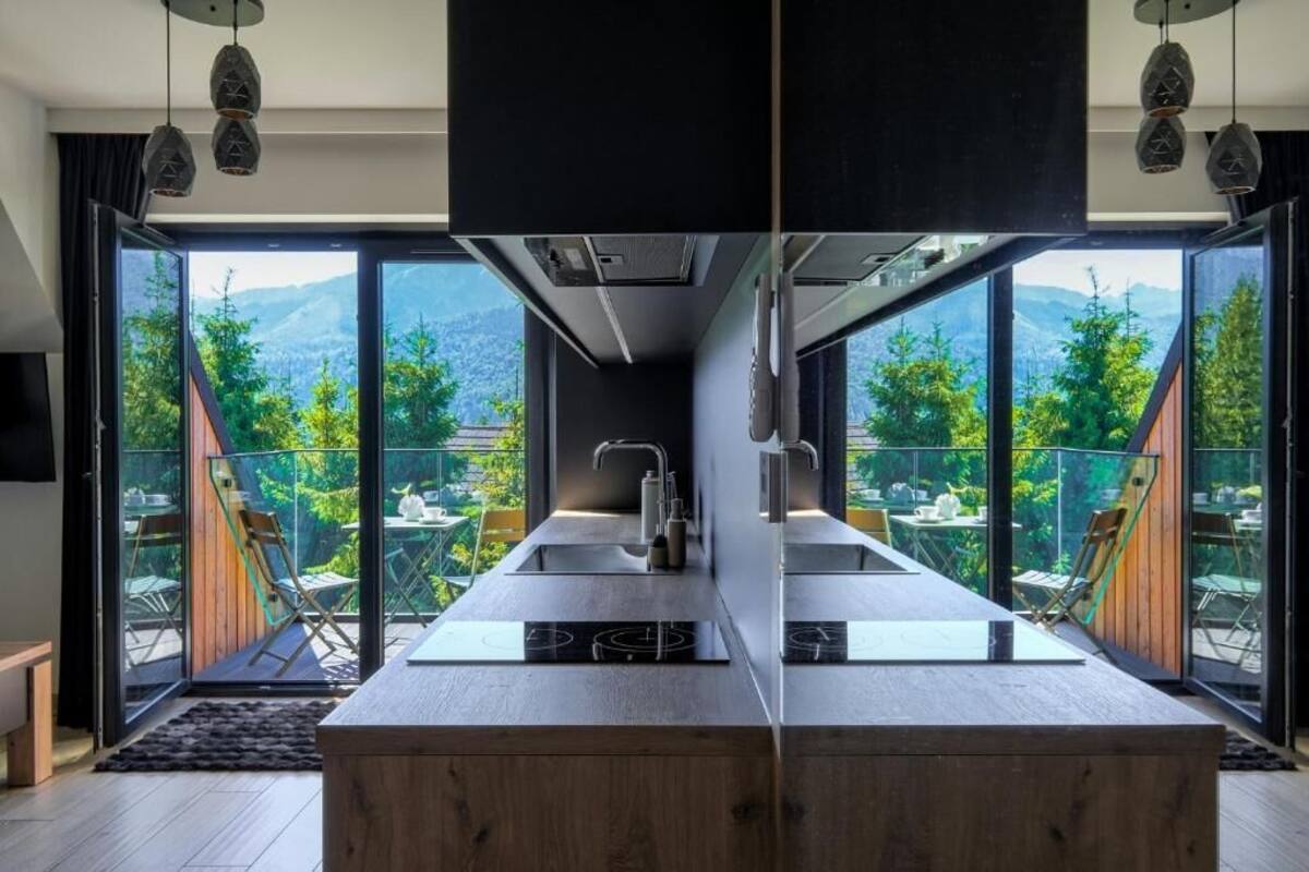 A modern kitchen with a central island, two sinks, and a view of a mountainous landscape through large glass doors.