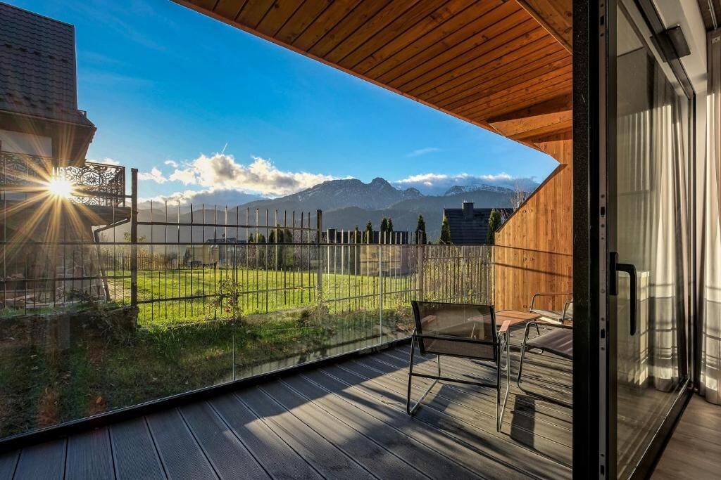 A balcony with a wooden floor, a glass door, and a view of a mountain range.