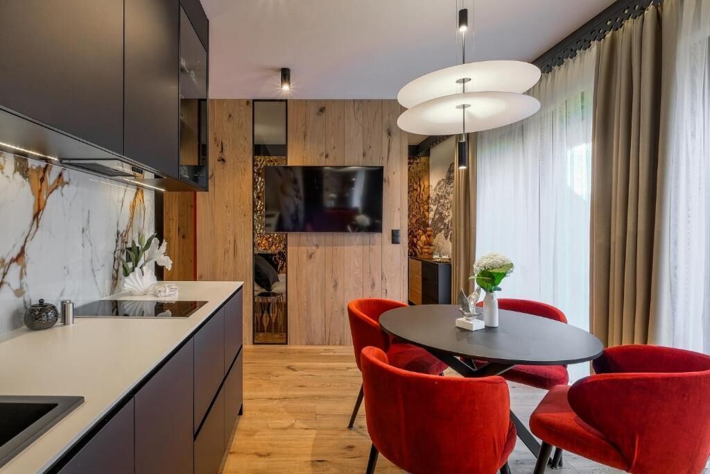 Een moderne keuken met een ingebouwde oven, een eethoek met rode stoelen en een groot raam met gordijnen.