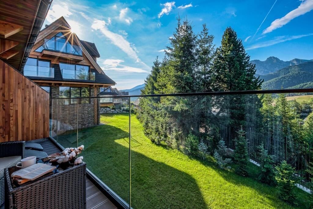 Una casa moderna con balcón de vidrio que da a un exuberante paisaje verde y montañas.