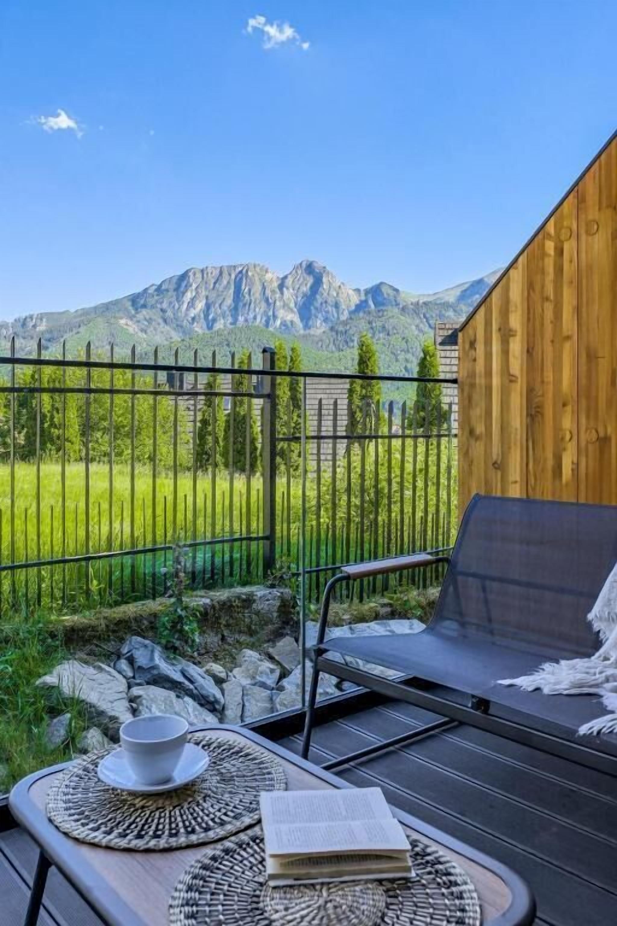 Un balcón con vistas a montañas, un muro de madera y una mesa con un libro y una taza.