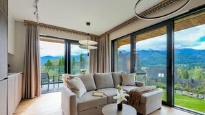 Ein modernes Wohnzimmer mit einer Couch, einem runden Couchtisch und Blick auf Berge durch große Fenster.