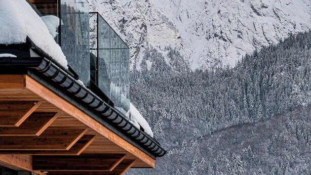 Eine Bergingerhütte mit einem Holzbalkon mit Blick auf einen schneebedeckten Berg.