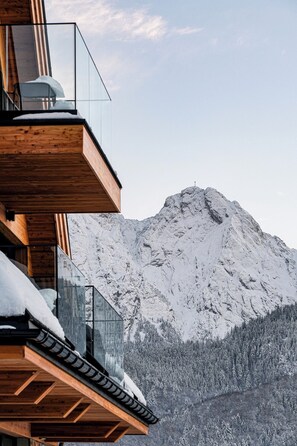 A mountain cabin with a wooden balcony overlooking a snow-covered mountain.