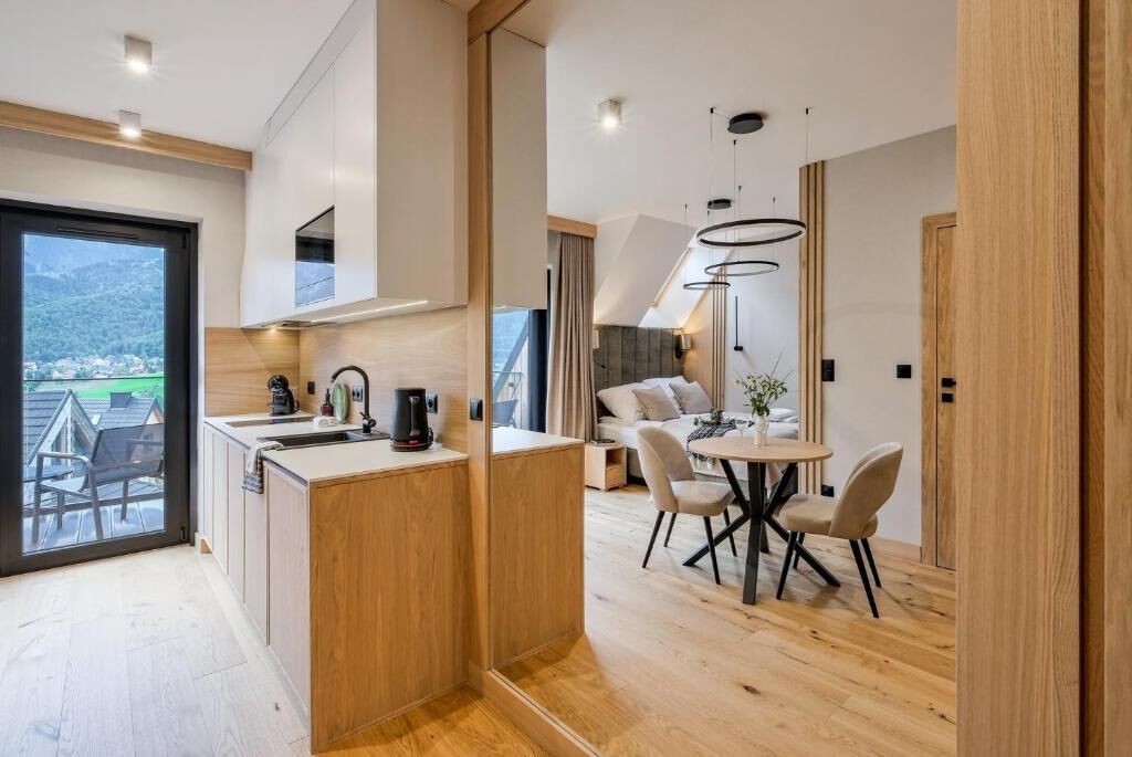 Et moderne køkken med en central ø, et spiseområde med et rundt bord og udsigt til et bjergrigt landskab gennem et stort vindue.
