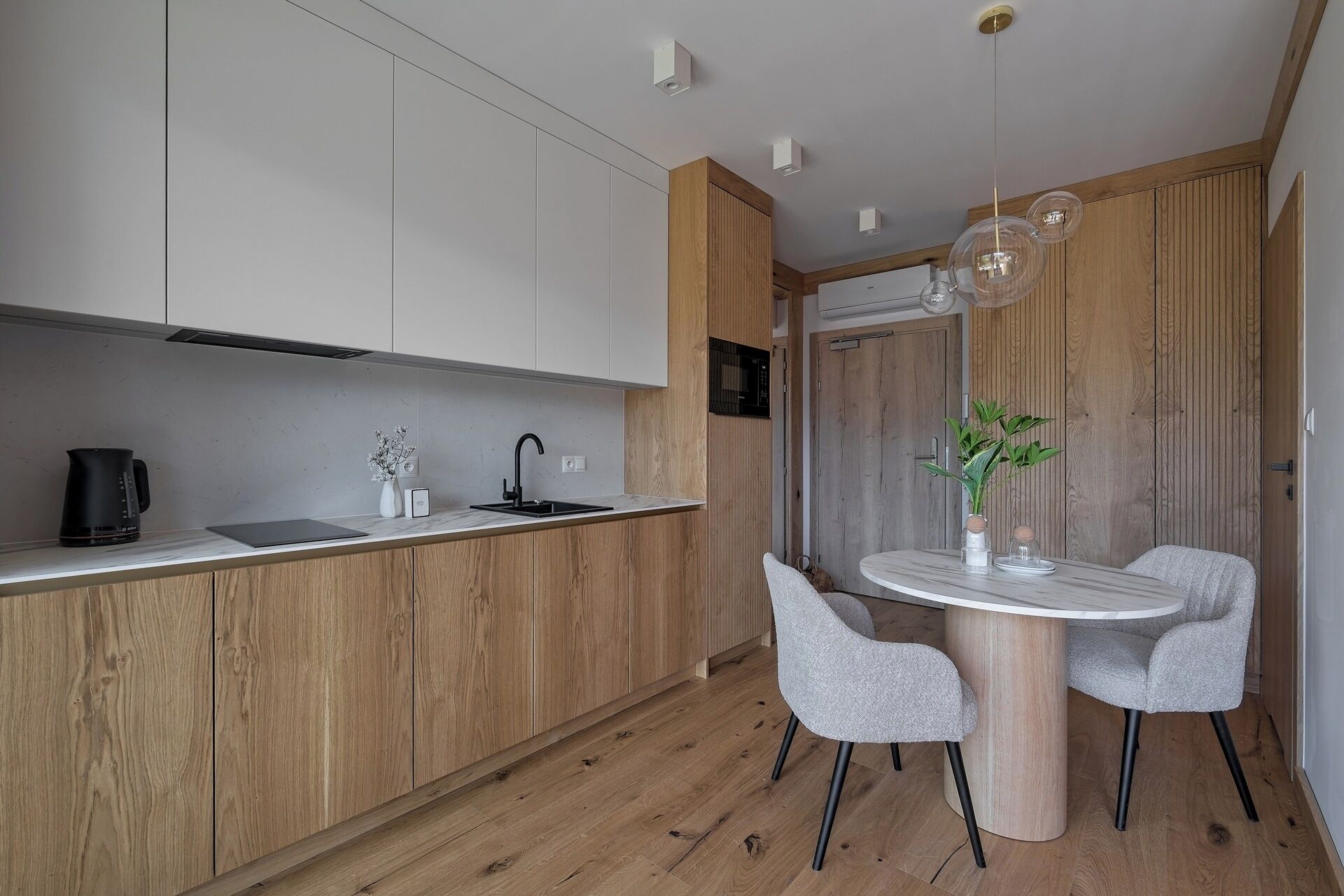 A modern kitchen with wooden cabinets, a built-in oven, and a dining area with a round table and two chairs.