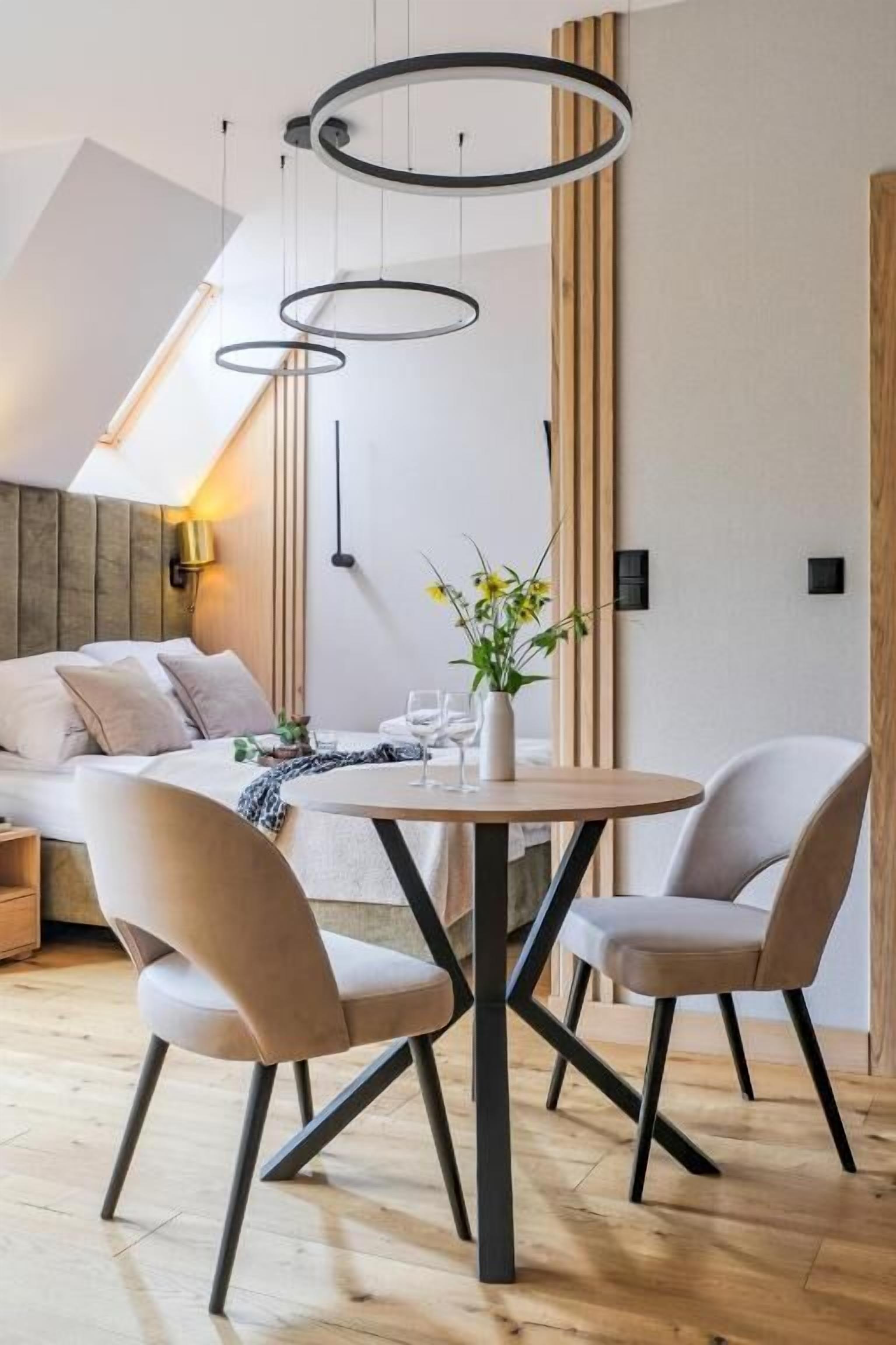 A modern dining area with a round table, two chairs, and a pendant light fixture.