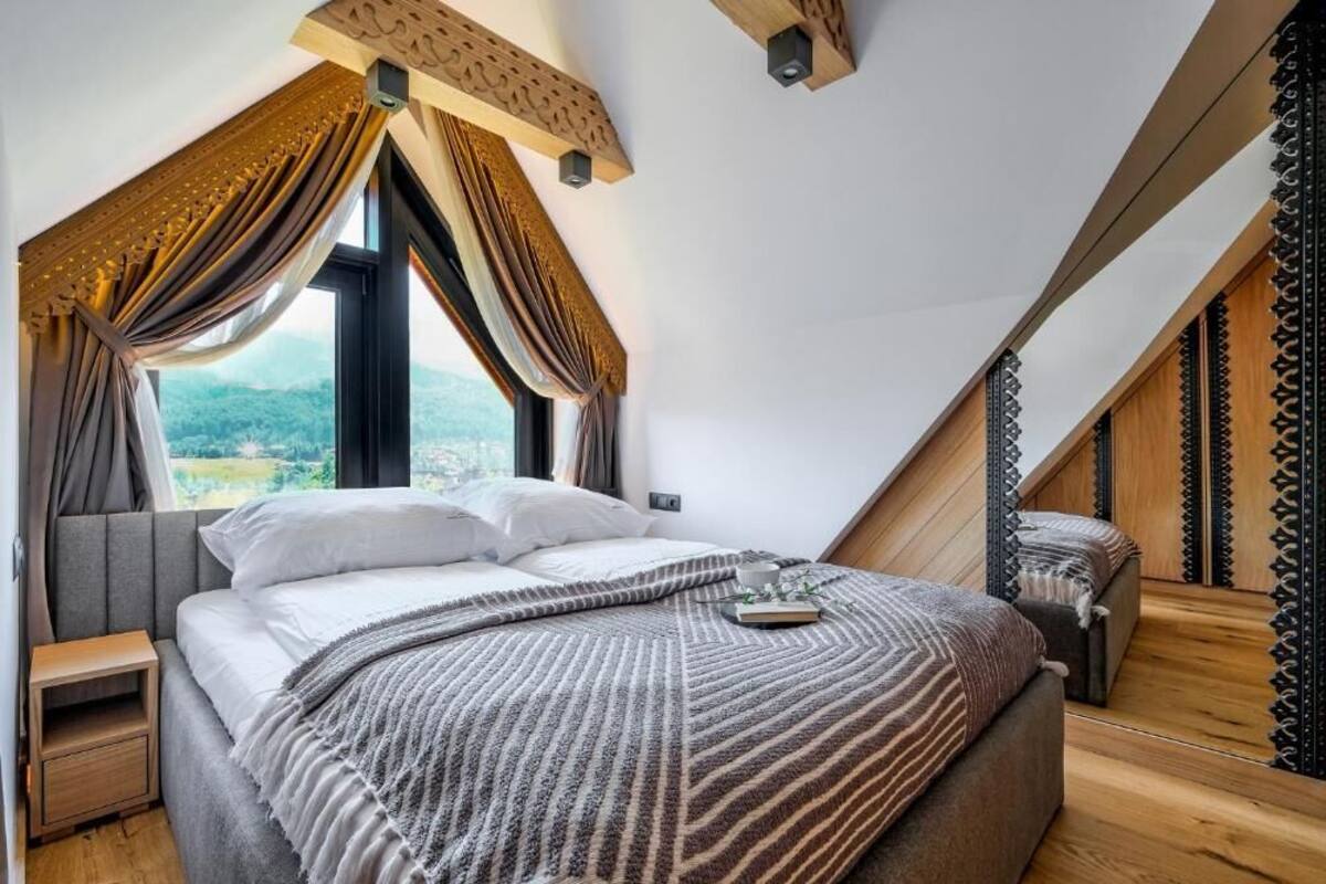 A bedroom with a bed, a nightstand, and a window with curtains.