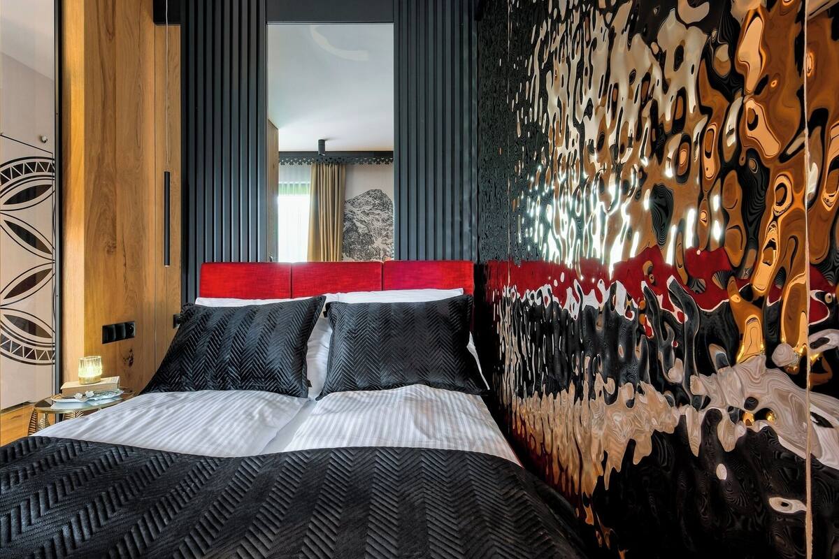 A modern hotel room with a large bed, a red headboard, and a unique abstract wall design.