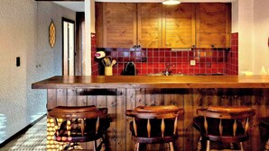 Een keuken met houten kastjes, een backsplash van rode tegels, en een bar met krukken.