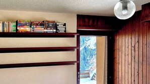 Een slaapkamer met een bed, een houten stoel, een boekenkast en een raam met uitzicht op een besneeuwd landschap.