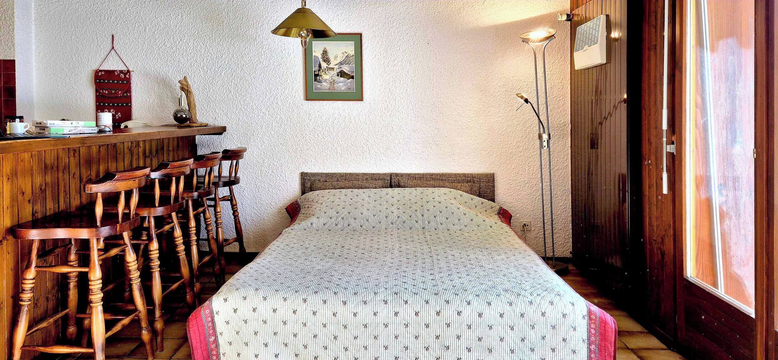 Ein gemütliches Zimmer mit einer Holztrennwand, einem Bett mit gemustertem Überwurf, einem gerahmten Bild an der Wand und einer hohen Stehlampe.