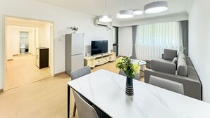 A modern living room with a sofa, a dining table with chairs, a TV, and a kitchen area with a refrigerator and a microwave. - Tyms Gubei 2BR Apt near Gubei Road (Shanghai)