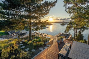 Un pontile in legno con posti a sedere all'aperto, una piccola piscina e vista sul tramonto sull'acqua.