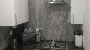 A modern kitchen with a gas stove, a coffee maker, and a microwave. - Modern & Stylish Retreat  15 Mins to Central London (Barking)